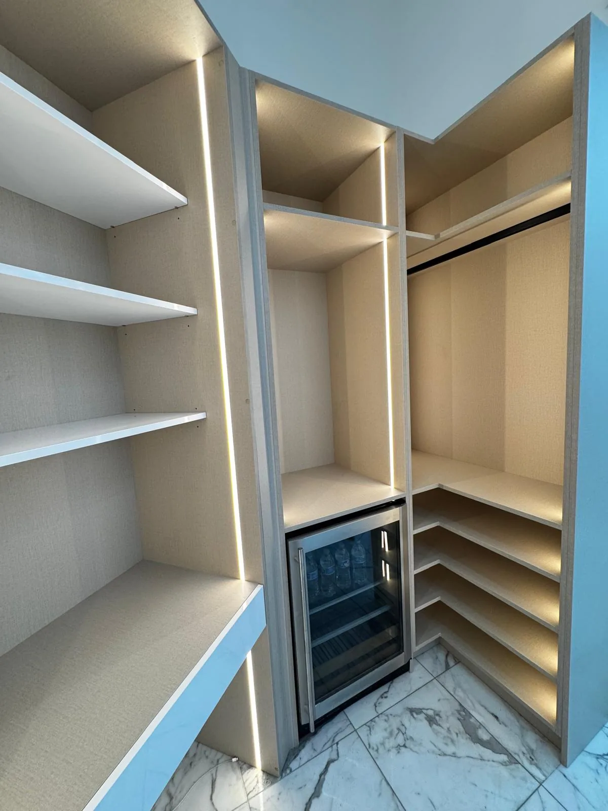 Boutique walk-in closet with LED lighting and beverage fridge by Decoart
